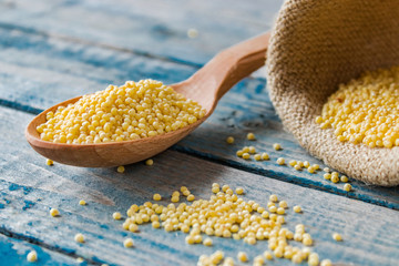 A wooden spoon with millet lies near a bag of millet against the background of old blue boards.