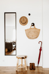 Bright modern Scandinavian interior design. Living room with mirror, stool, hat, straw bag, umbrella and shoes.