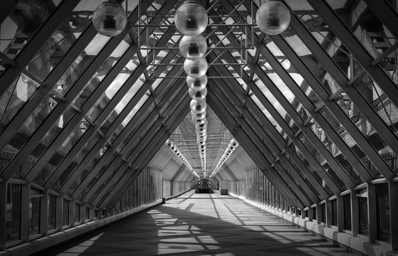 Black and white image of a pedestrian bridge with a triangular roof and round lampshades