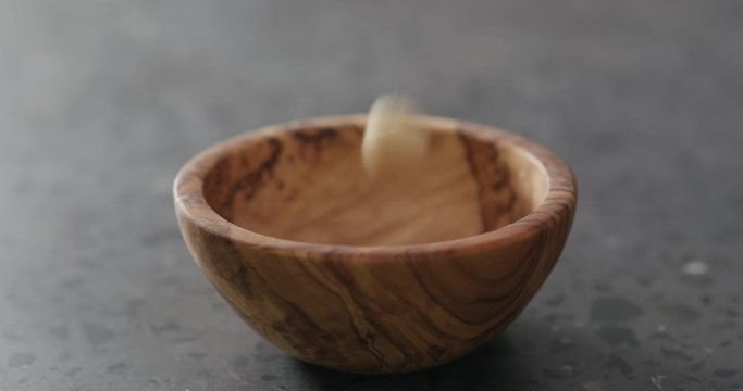 Slow motion peeled macadamia nuts fall into olive wood bowl