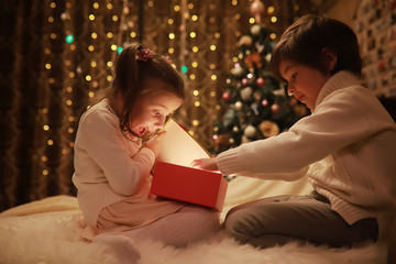 Family on Christmas eve at fireplace. Kids opening Xmas presents. Children under Christmas tree...