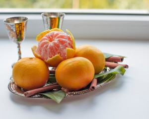 Tangerines with leaves and cinnamon stick on a silver or metal tray or platter with silver glasses on a white windowsill