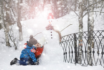 Children in the park in winter. Kids play with snow on the playground. They sculpt snowmen and slide down the hills.