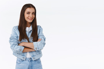Attractive sassy brunette girl in denim jacket, jeans, cross arms over chest, standing half-turned,...