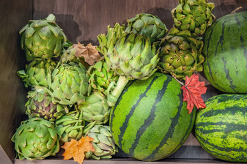 Fototapeta premium Farm vegetables ripe watermelons and artichokes lie in a box in the window of the farmers market. The latest varieties and hybrids of fruits and vegetables