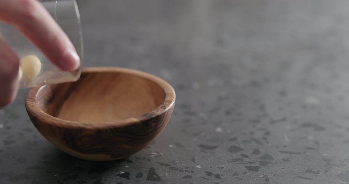 Slow motion peeled macadamia nuts fall into olive wood bowl