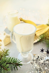 Irish traditional winter cream cocktail eggnog in a glass mug with milk, rum and cinnamon, banana covered with whipped cream, Christmas decorations.