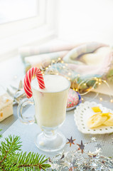 Irish traditional winter cream cocktail eggnog in a glass mug with milk, rum and cinnamon, banana covered with whipped cream, Christmas decorations.