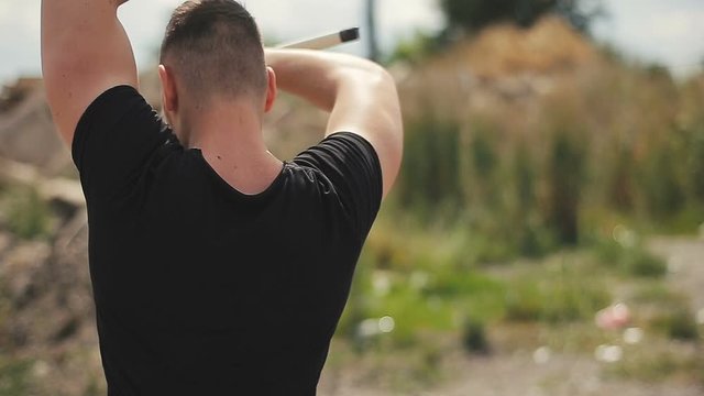 Handsome young man in black t-shirt demonstrates skill with nunchaku outdoors.