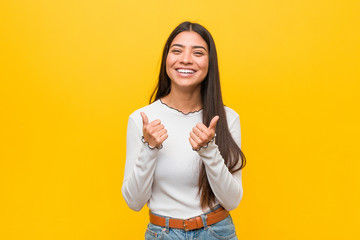 Young pretty arab woman against a yellow background raising both thumbs up, smiling and confident.