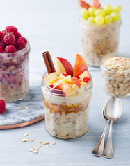 Overnight oats, bircher muesli with raspberry, apple in glass jars on wooden background.