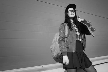 A young hipster girl is riding a skateboard. Girls girlfriends for a walk in the city with a skateboard. Spring sports on the street with a skateboard.