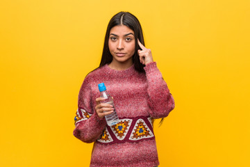 Young arab woman holding a water bottle pointing his temple with finger, thinking, focused on a task.