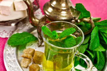 Moroccan tea with green mint and dessert on a pink textile background