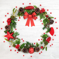 Christmas wreath with red bow, bauble decorations, winter flora and loose holly berries on rustic wood background.