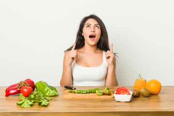 Young curvy woman preparing a healthy meal pointing upside with opened mouth.