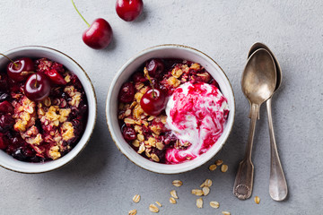 Cherry, red berry crumble with ice cream in bowls. Grey stone background. Top view.