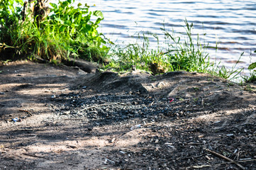 Fireplace in forest near water with garbage left after campers