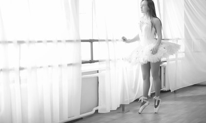 Young ballet dancer on a warm-up. The ballerina is preparing to perform in the studio. A girl in ballet clothes and shoes kneads by the handrails.