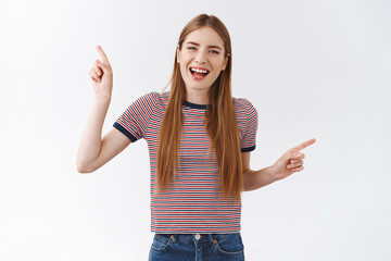 Joyful, positive alluring young student girl in striped t-shirt cheerfully pointing sideways, indicate left and right, smiling entertained and upbeat, promote two products, give suggestions