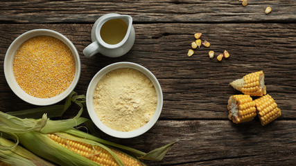 Corn oil, polenta corn grits, corn flour in a porcelain bowl on a wooden table. Ears of corn and slices of corn next to bowls. Gluten free healthy foods.