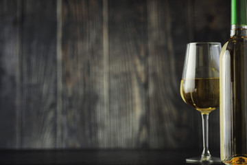 Transparent bottle of white dry wine on the table. White wine glass on a wooden background.