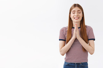 Hopeful, positive cute european woman in striped t-shirt hold hands in pray, smiling nervously and...