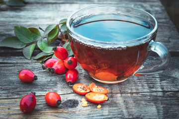 A cup of rosehip tea near red berries on a wooden table.
