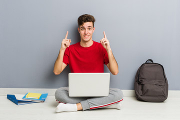 Young student man sitting on his house floor holding a laptop