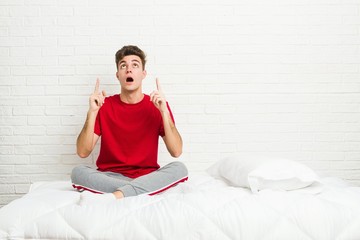 Obraz premium Young teenager student man on the bed pointing upside with opened mouth.