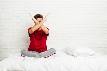 Young teenager student man on the bed keeping two arms crossed, denial concept.