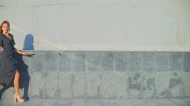 stylish lady with long loose flowing hair walks near concrete wall sideways casting grey shadow slow motion