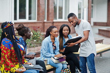Fototapeta Group of five african college students spending time together on campus at university yard. Black afro friends studying at bench with school items, laptops notebooks. obraz