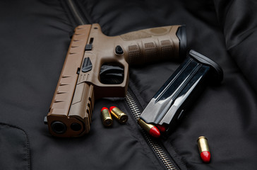 A modern brown pistol and ammunition on it are on a dark jacket. Weapons for police, army, special forces.