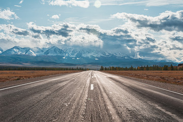 Panorama of mountain road of on background of beautiful snowy mountain peaks in cloudy weather. Mountain highway. View of trail on the background of blue sky