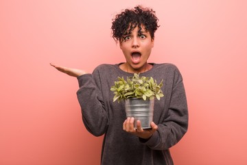 Young african american woman holding a plant cheerful and confident showing ok gesture.