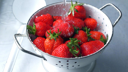 Sieb mit frischen Erdbeeren werden gewaschen mit Wasser unter fließendem Wasserhahn