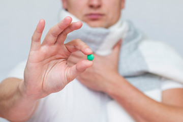 man holds a green pill between his fingers, treatment pill, hold on to the throat, sore throat