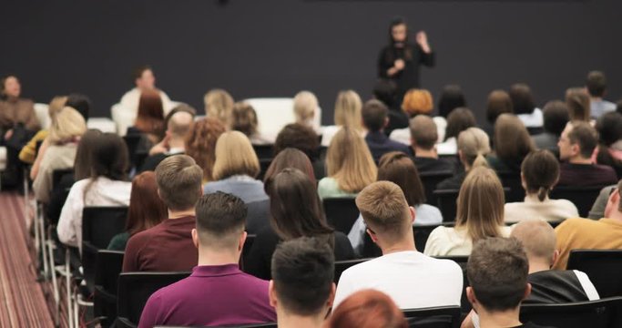 Conference, seminar, training, coaching in group. Public speech concept. Educational finance lectures for startuppers. Business forum with woman speaker talking in large audience, view from viewers.