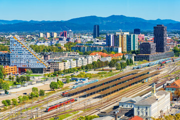 Aerial panorama of Ljubljana with modern buildings, the main train station, trains and beautiful green hills in the background, Slovenia