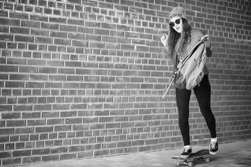 Fototapeta na wymiar A young hipster girl is riding a skateboard. Girls girlfriends for a walk in the city with a skateboard. Spring sports on the street with a skateboard.