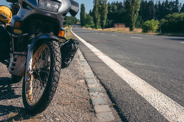 Fototapeta premium The old adventure motorcycle on the side of the road. The concept of a long trip on a tourist bike. asphalt road, place for text.