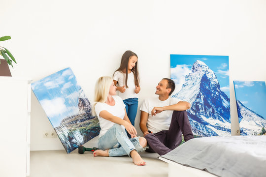 In new flat family hangs a large photo canvas on empty white wall at home
