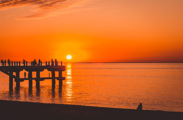 Colorful sunset at the sea and a pier with fishermen.