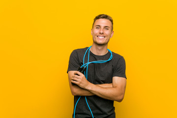 Young caucasian man holding a jump rope smiling confident with crossed arms.