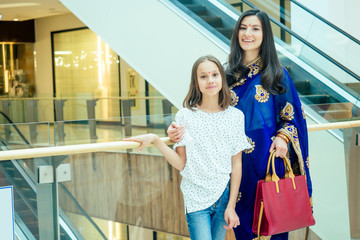 Portrait of a young indian woman wearing blue sari and gold bracelet having fun with her cute daughter in shopping mall,escalator background.red religious dot on forehead