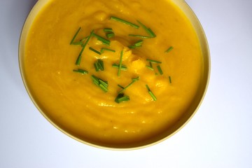 Pumpkin soup and chives in ceramic plate on light background.