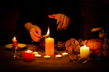 Witch burns a herb on the altar in the dark. Female hands with sharp black nails do magic among...