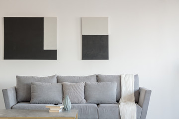 Abstract black and white painting on empty wall of stylish living room interior with comfortable grey couch with pillows