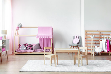 Fototapeta premium Copy space on empty white wall in stylish pink and bright baby room with wooden furniture